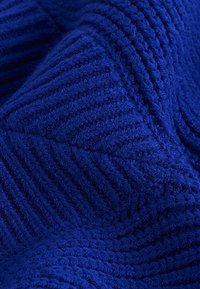 Close-up van diepblauwe textuurstof met verhoogde geometrische chevron- en diagonale lijnpatronen.