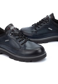 Zapatos de piel negra con un acabado suave, diseño con cordones, suela de goma, cuello acolchado y detalles de marca en la lengua y el lateral.