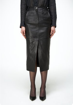 Sort lædermidi-nederdel med frontslids båret med gennemsigtige sorte strømper og sorte spidse hæle.