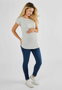 Tehotenský top v šedých a bielych prúžkoch, s krátkymi rukávmi, v kombinácii s tmavomodrými skinny džínsami a bielymi teniskami, so zaobleným lemom.