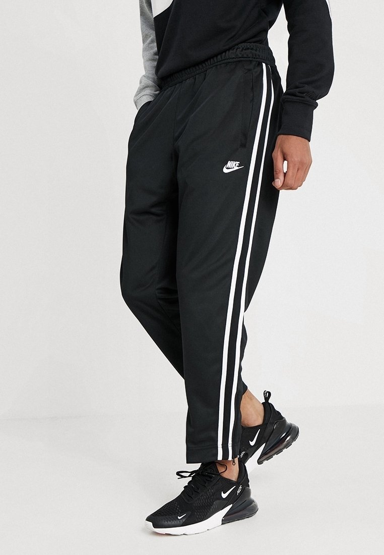 Personen bär svarta Nike träningsbyxor med vita sidostrecker och svarta Nike sneakers med vita sulor och logotyper.