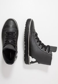 Czarne buty typu high-top wykonane z teksturowanego materiału syntetycznego, z gumową podeszwą, białymi paskami akcentującymi i okrągłymi metalowymi oczkami.