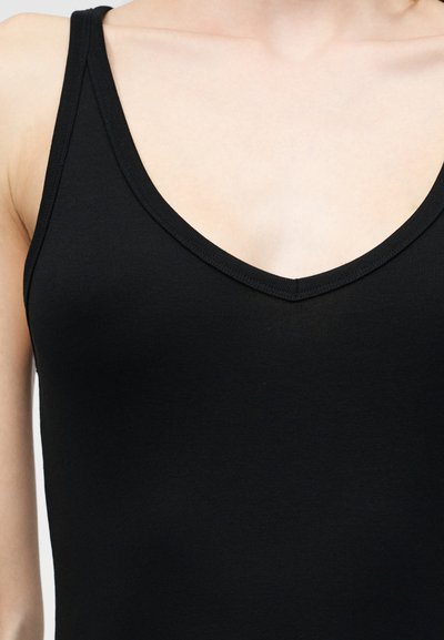 Κοντινό πλάνο ενός ατόμου που φοράει μαύρο βαμβακερό αμάνικο τοπ με V-λαιμόκοψη.