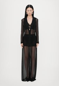 Schwarzes, durchsichtiges langes Kleid mit gefüttertem Oberteil, tiefem Ausschnitt und langen Ärmeln, das über einer Spitzenunterwäsche getragen wird und minimalistische Details aufweist.