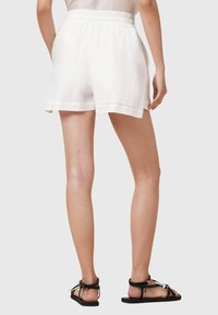 Pantaloni corti bianchi e leggeri con una vita elastica, caratterizzati da un fit rilassato e una texture liscia. Abbinati a sandali neri con fasce.