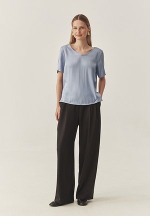 Top azzurro chiaro a maniche corte con scollatura a V e orlo curvo, abbinato a pantaloni neri larghi. Il tessuto appare liscio e leggero.