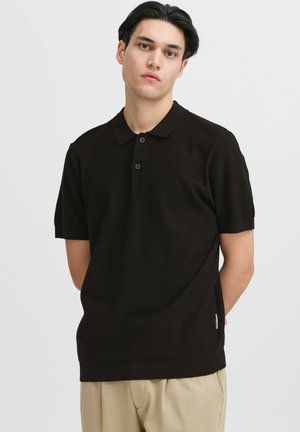 Black short-sleeve polo shirt with a classic collar, three-button placket, and subtle textured fabric; featured with a small side tag detail.
