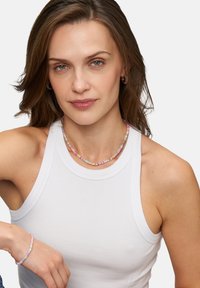 Farverig perlekæde med pastelnuancer, der har små cylindriske perler og et matchende armbånd. Model iført en ærmeløs hvid top.