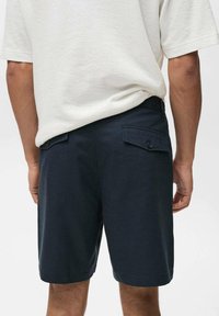 Pantaloni scurți bleumarin dintr-un material cu textură netedă, având două buzunare la spate cu închidere prin buton și o croială ajustată.