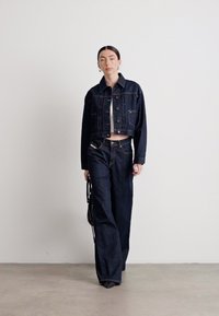 Mørk denimjakke med en kort design, kombinert med løse mørke bukser. Minimalistisk stil med en lys topp og svart veske.