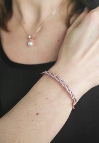 Bracciale in oro rosa con design intrecciato decorato con cristalli chiari, che presenta una texture liscia e una finitura riflettente.