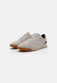 Lys grå ruskinnsneakers med gummisåler, runde tær og kontrasterende svarte detaljer. Har tynne lisser og subtil preget dekor.