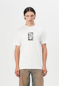 Hvid bomulds-t-shirt med et rektangulært sort-hvidt grafisk print i midten, rund halsudskæring og korte ærmer.