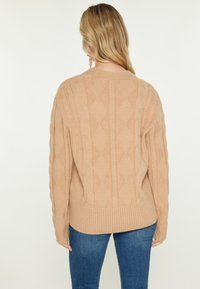 Beige kötött pulóver gyémántmintával, bordázott aljjal és hosszú ujjakkal. Puha tapintású, közepes hosszúságú dizájn, amely rétegezéshez ideális.