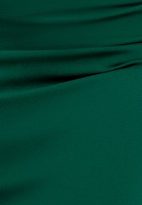 Vihreä kangas, jolla on sileä pinta, sisältää hienovaraisia laskoksia ja taitoksia. Materiaali näyttää kevyeltä ja pehmeältä.