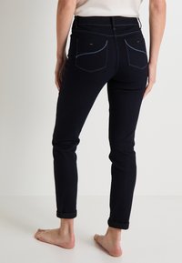 Jeans de denim navy con un corte ajustado, puños enrollados, bolsillos traseros y detalles de costura en contraste. El material parece suave con un ligero estiramiento.