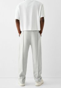 White cropped t-shirt paired with light grey, relaxed-fit sweatpants featuring side pockets and a smooth texture. Rubber-soled footwear.