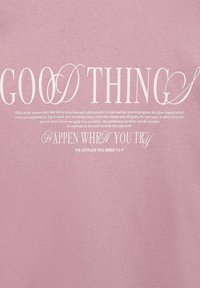 Světlá růžová bavlněná látka s bílým textem. Výrazné fráze zahrnují "DOBRÉ VĚCI" a "SE DĚJÍ, KDYŽ SE SNAŽÍTE," s různými styly písma.