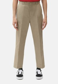 Beige high-waisted pants with a straight leg design, featuring pleats and side pockets, paired with black sneakers and white laces.