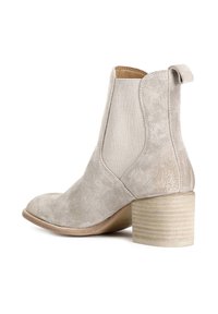 Stivale alla caviglia in suede beige con punta arrotondata, pannelli laterali elastici e tacco in legno impilato texturizzato. Include un occhiello sul retro.