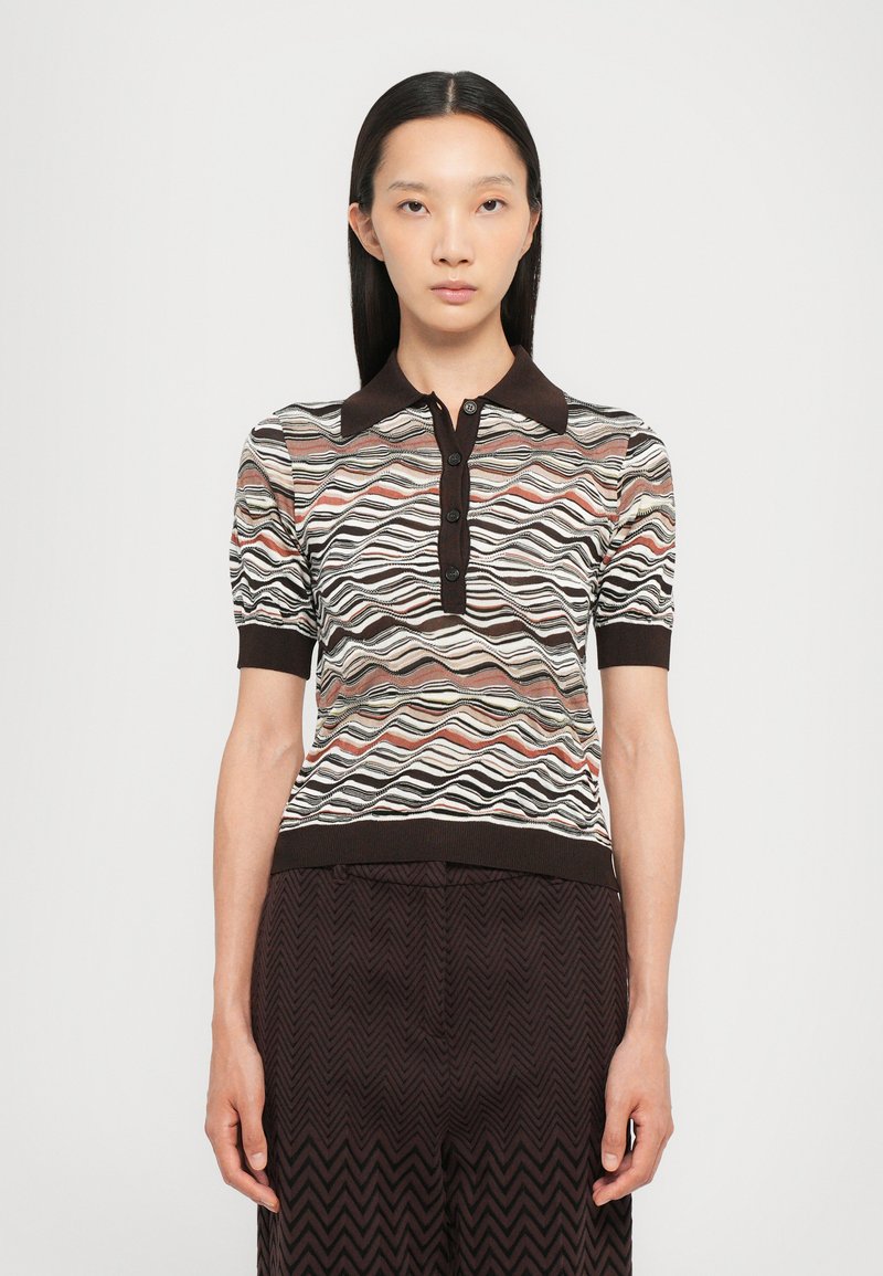 Knit polo shirt with a wave pattern in muted colors, brown collar, and five-button placket. Worn with dark patterned trousers.