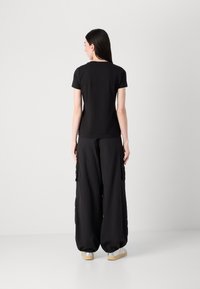 Must täpsega must t-särk, mis on ühendatud lõdva musta cargo-pükste paariga. Riietus sisaldab lühikesi varrukaid, lihtsat disaini ja mugavat siluetti.