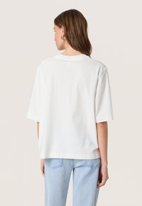 Bílý bavlněný tričko s krátkým rukávem, volný střih a kulatým výstřihem. Jednoduchý design, hladká textura bez viditelných vzorů nebo akcentů.