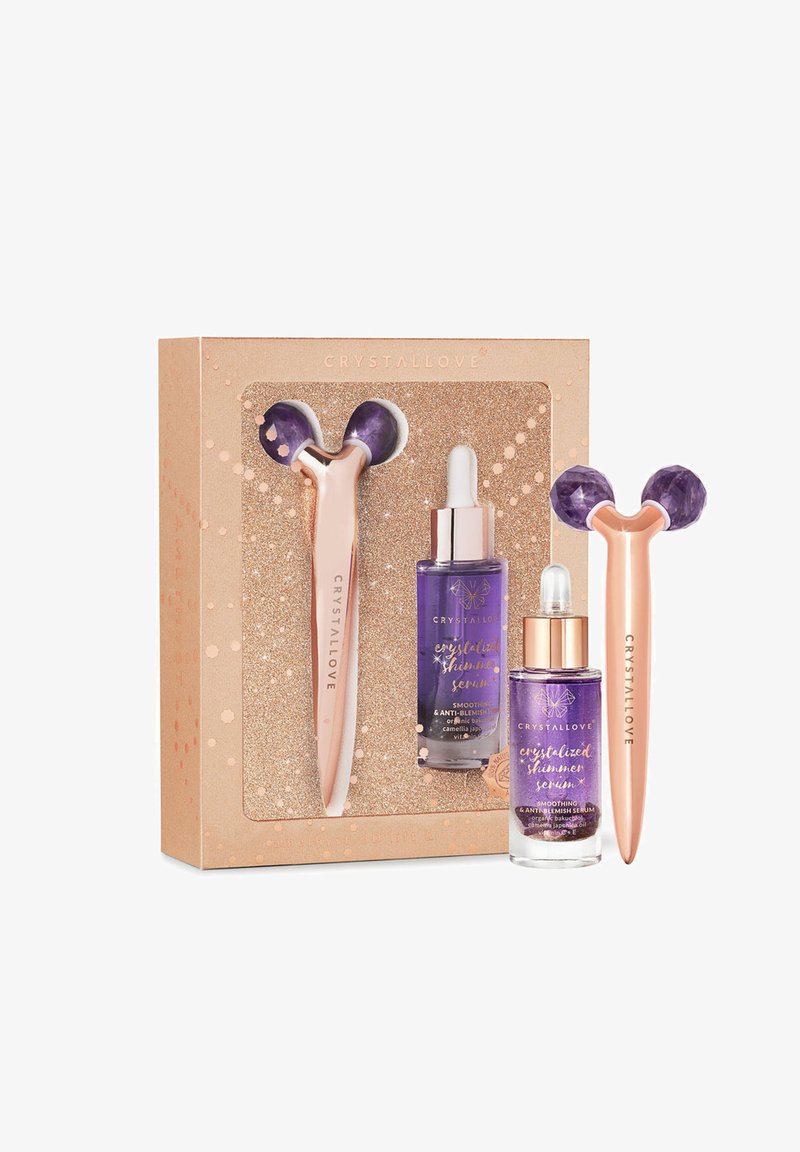 Zestaw prezentowy CrystalLove zawierający fioletowy wałek do twarzy ze złotą różową rączką oraz dwie fioleczki fioletowego serum w błyszczącym złotym pudełku.