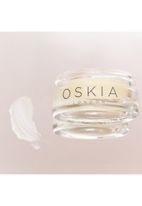 Crema Oskia London in un barattolo di vetro trasparente con una texture liscia e giallo pallido, accompagnata da una striscia di crema su una superficie riflettente.