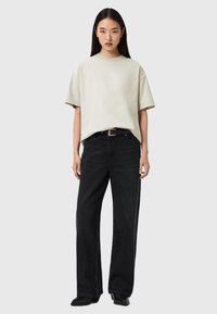 Μπεζ φαρδιά κοντομάνικη μπλούζα, μαύρο τζιν ψηλόμεσο, μαύρη ζώνη και μαύρα παπούτσια. Λείο ύφασμα με άνετη εφαρμογή, σχέδιο με ίσια γραμμή στα πόδια.