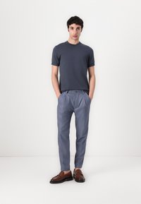 Pánský outfit zahrnující šedé tričko, světle modré skládací kalhoty a hnědé kožené mokasíny. Jednoduchý design, přiléhavý střih a hladká textura.