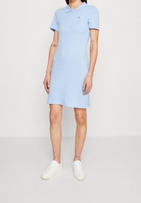 Lichtblauwe polojurk met korte mouwen, een kraag met knopen en een aansluitende pasvorm. Gecombineerd met witte sneakers voor een casual uitstraling.