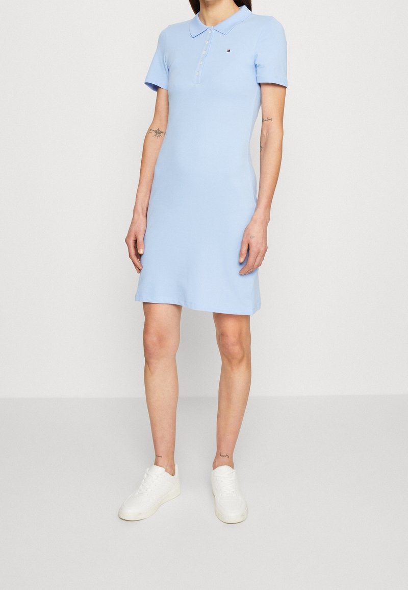 Lichtblauwe polojurk met korte mouwen, een kraag met knopen en een aansluitende pasvorm. Gecombineerd met witte sneakers voor een casual uitstraling.