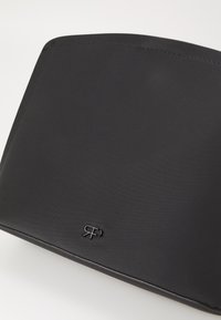 Zwarte portemonnee van gestructureerd synthetisch materiaal, met ronde hoeken en een reliëflogo in de rechterbenedenhoek.