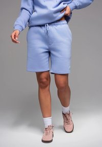 Pantaloni corti in misto cotone blu chiaro con vita elastica e cordino. Presentano tasche laterali e una patch con logo sulla coscia sinistra.