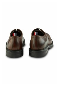 Chaussures en cuir marron avec une texture lisse et une forme arrondie. Présentent une semelle noire contrastante et un onglet tricolore à l'arrière.