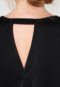 Top negro con un diseño de corte en la espalda que presenta una abertura rectangular. La tela tiene una textura suave, destacando un diseño minimalista.