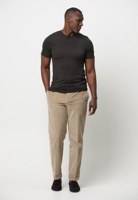 Mörkgrå kortärmad t-shirt i kombination med beige kordflöjelsbyxor med vertikala ränder. Svarta avslappnade skor fulländar outfiten.