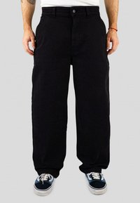 Black, wide-leg cargo pants made of cotton, featuring a button closure, side pockets, and a smooth texture. Paired with blue sneakers.