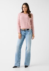Pull en tricot texturé rose clair avec un col rond, associé à un jean bleu clair à jambes larges et des talons noirs à bout pointu.