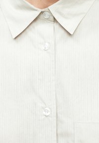 Chemise blanche à col avec fines rayures noires verticales et trois boutons transparents le long de la patte de boutonnage avant.