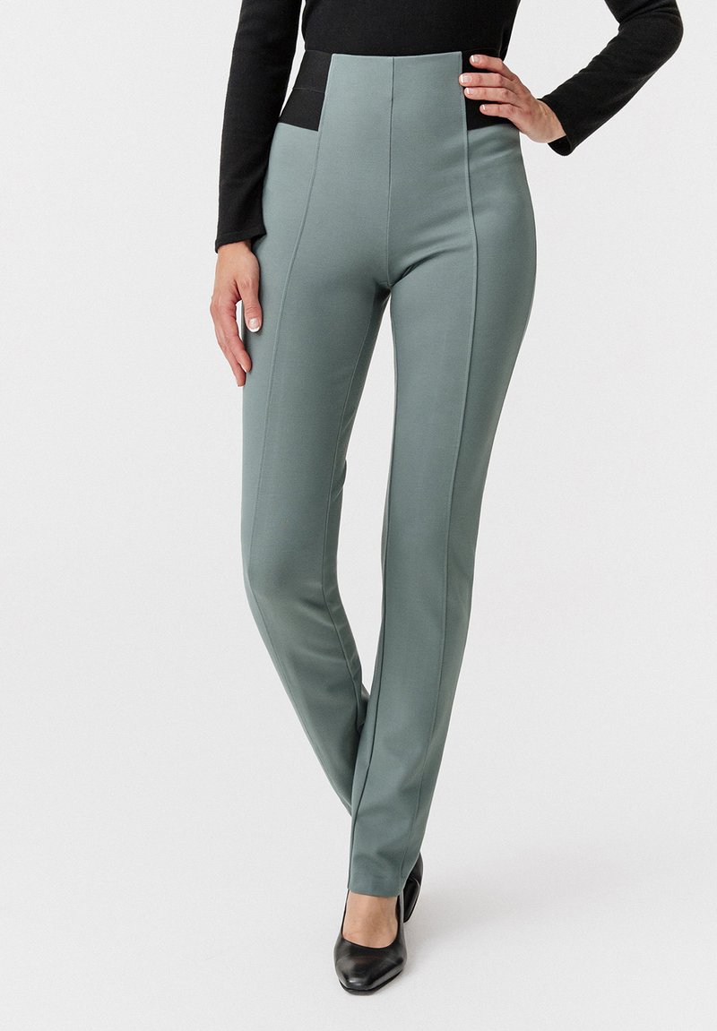 Pantaloni slim-fit a vita alta in tessuto verde chiaro con una texture liscia, caratterizzati da accenti neri sui lati e cuciture verticali per un look sartoriale.
