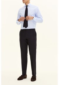 Vaaleansininen raidallinen paitapusero, musta solmio, tummat housut ja ruskeat mokkanahasta tehdyt loafersit. Räätälöity istuvuus teksturoidusta kankaasta ja klassisella kauluksella.