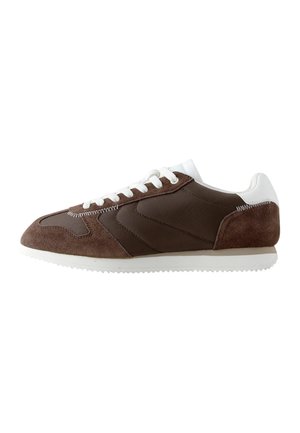 Brązowy i biały niski sneaker z panelami z zamszu i tkaniny, białe sznurówki oraz piłkowana biała gumowa podeszwa.