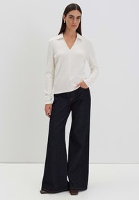 Weißer V-Ausschnitt-Pullover mit langen Ärmeln, kombiniert mit dunkelblauen, weiten Jeans. Der Stoff wirkt glatt, ohne erkennbare Muster oder Verzierungen.