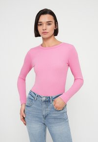 Ροζ μακρυμάνικη μπλούζα με εφαρμοστή σχεδίαση και φαρδιά λαιμόκοψη, σε συνδυασμό με ανοιχτό μπλε ψηλόμεσο τζιν. Το ύφασμα φαίνεται ριμπ.