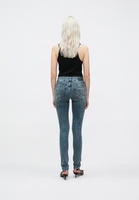 Ανοιχτό μπλε skinny τζιν παντελόνι από ντένιμ, με κλασικό σχέδιο πέντε τσέπες και διακριτική φθορά. Φορεμένο με μια μαύρη μπλούζα και ψηλές γόβες.