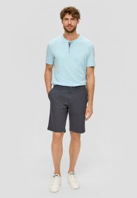 Chemise henley à manches courtes bleu clair, shorts gris et baskets blanches. La chemise présente une patte de boutonnage et une coupe décontractée.