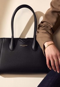 Schwarze Lederhandtasche mit strukturierten Oberflächen, doppelten Griffen und goldenem Logo "ISABEL BERNARD PARIS." Kombiniert mit einem braunen Ärmelschutz und Schmuck.