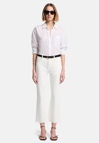 Witte blouse met lange mouwen en een borstzak, gecombineerd met witte flared jeans. Een zwarte riem en zwarte hoge sandalen maken de outfit compleet.